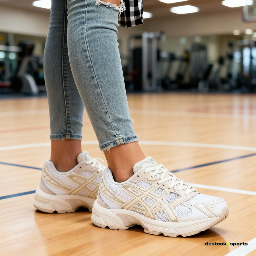 Une femme en jean porte des Asics blanc crème sur le parquet d'un gymnase